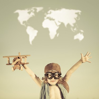 Happy kid playing with toy airplane against blue summer sky background.