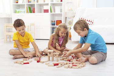 Three kids playing with wooden blocks sitting on the floor